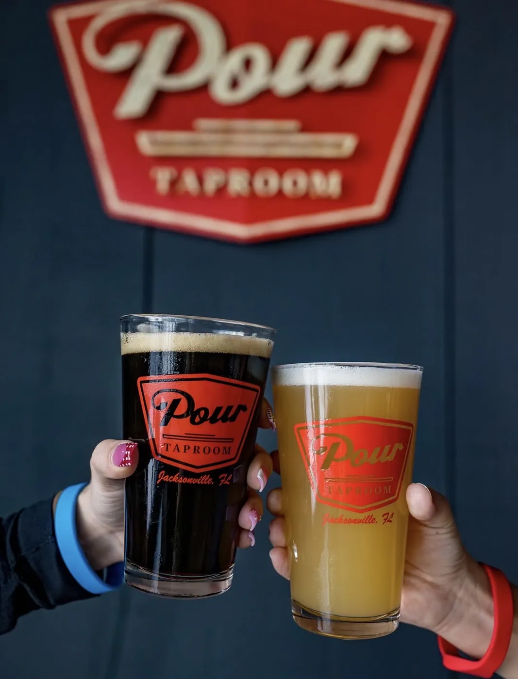 Two self-pour beers raised under the Pour Taproom sign